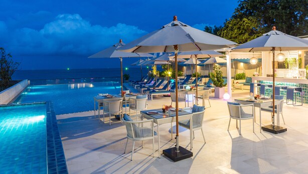 A poolside area with lounge chairs and umbrellas, a bar, and a view of the ocean. - The Rock Hua Hin Beachfront Spa Resort (Hua Hin)