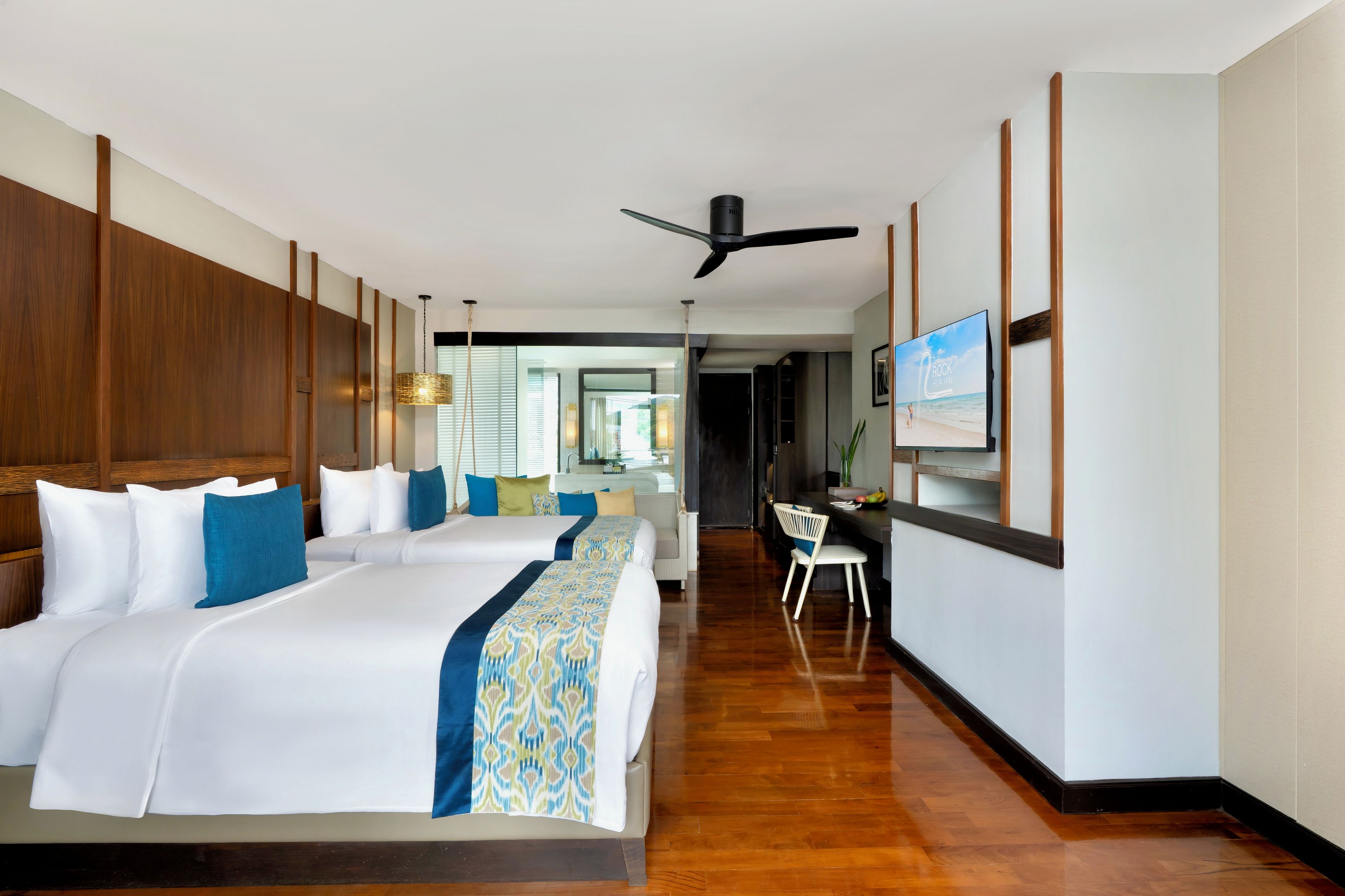 A hotel room with a large bed, a desk, a television, and a view of the beach.