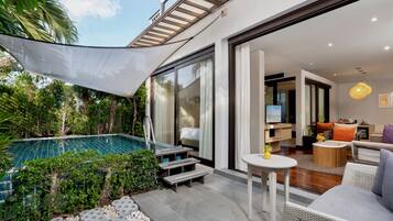 Un área de piscina moderna al aire libre con cerramiento de vidrio, rodeada de follaje y una zona de estar cubierta con una mesa y sillas pequeñas.