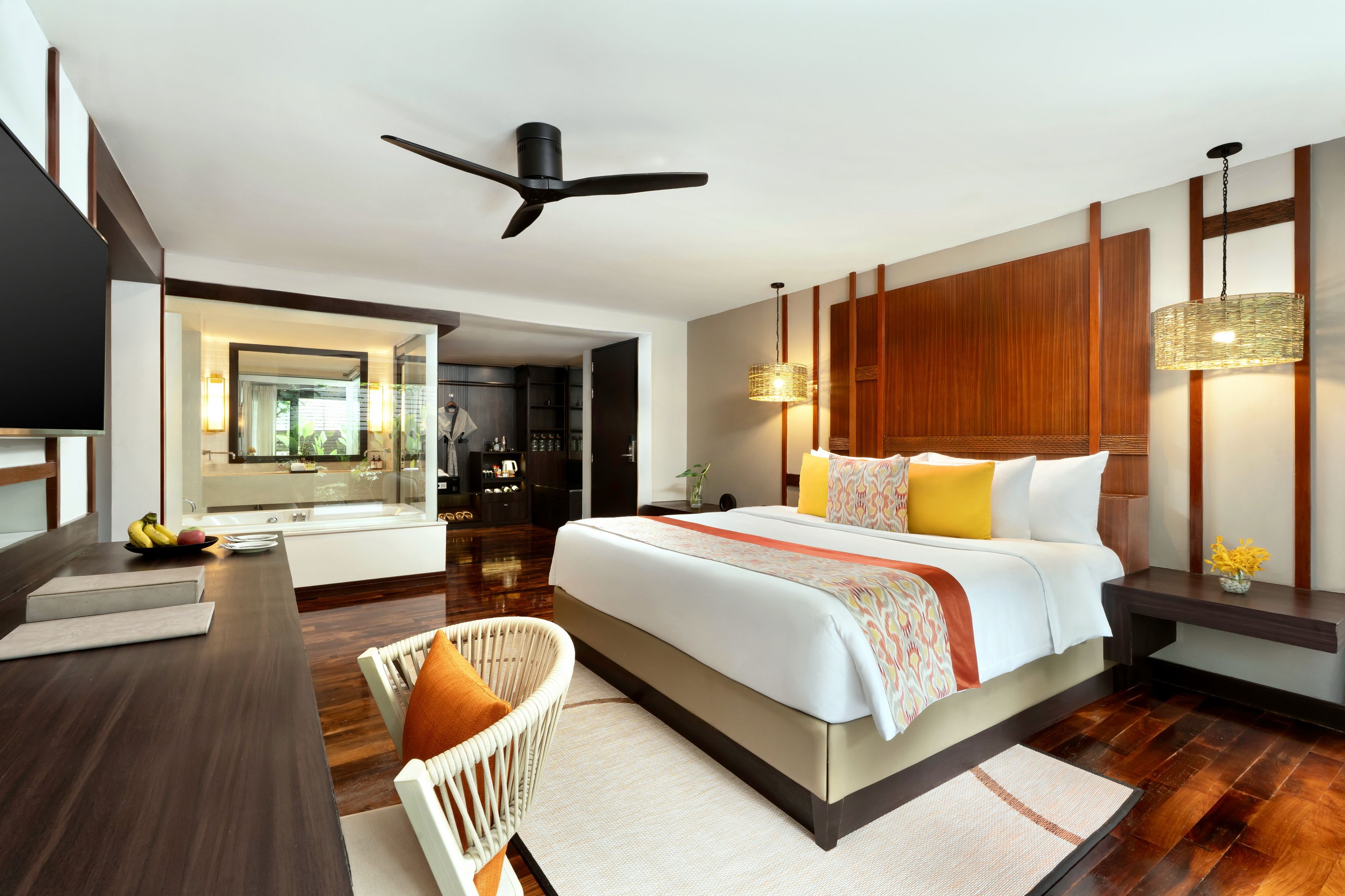A modern hotel room with a large bed, a desk, a chair, a ceiling fan, and a bathroom visible through an open door.