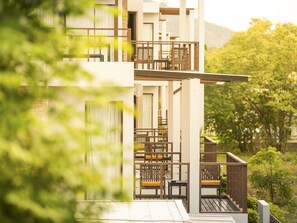 En modern byggnad med flera våningar, balkonger, utomhusmöbler och frodig grönska i bakgrunden.