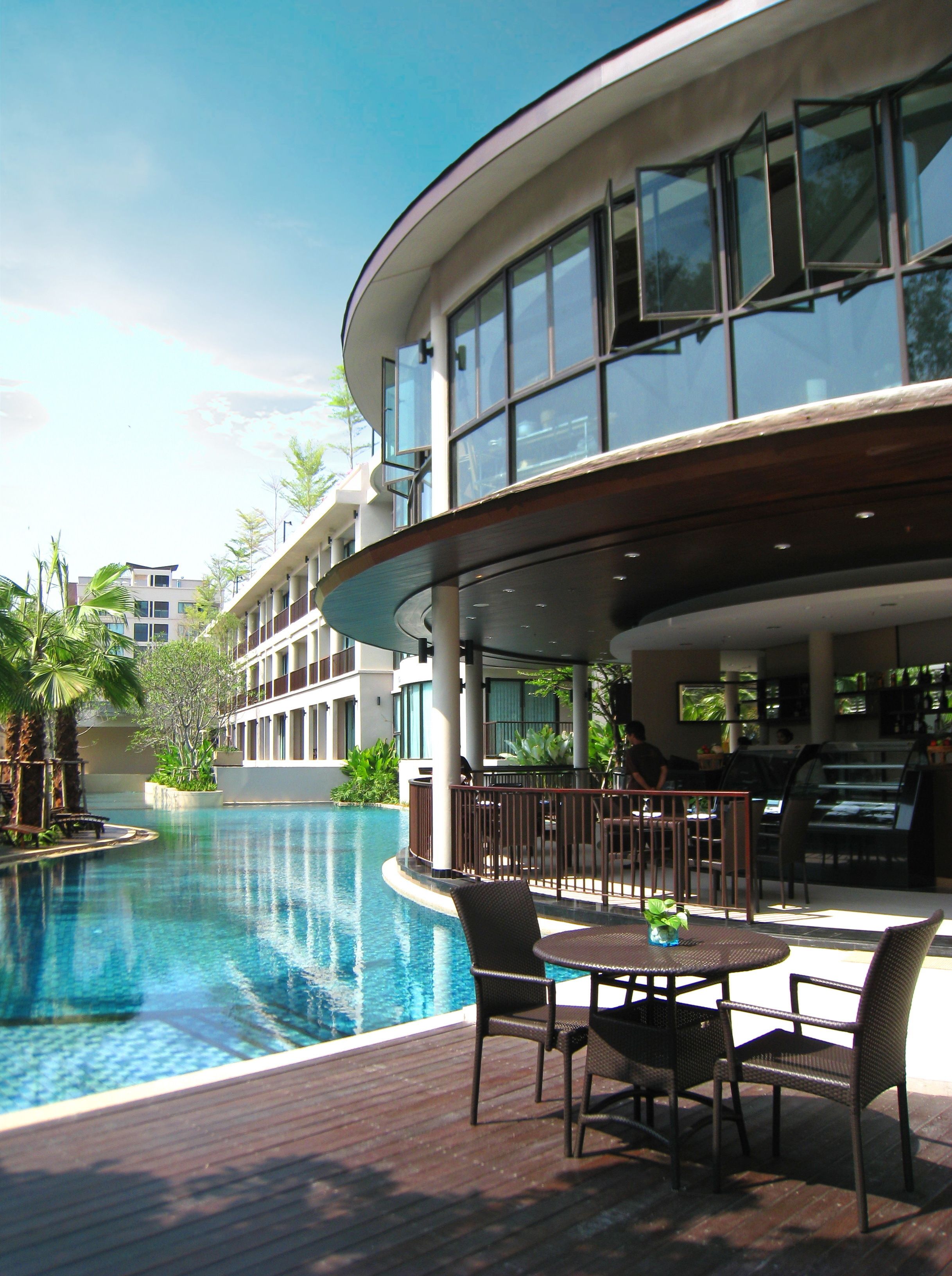 A poolside area with a wooden deck, outdoor seating, and a view of a modern building with large windows.