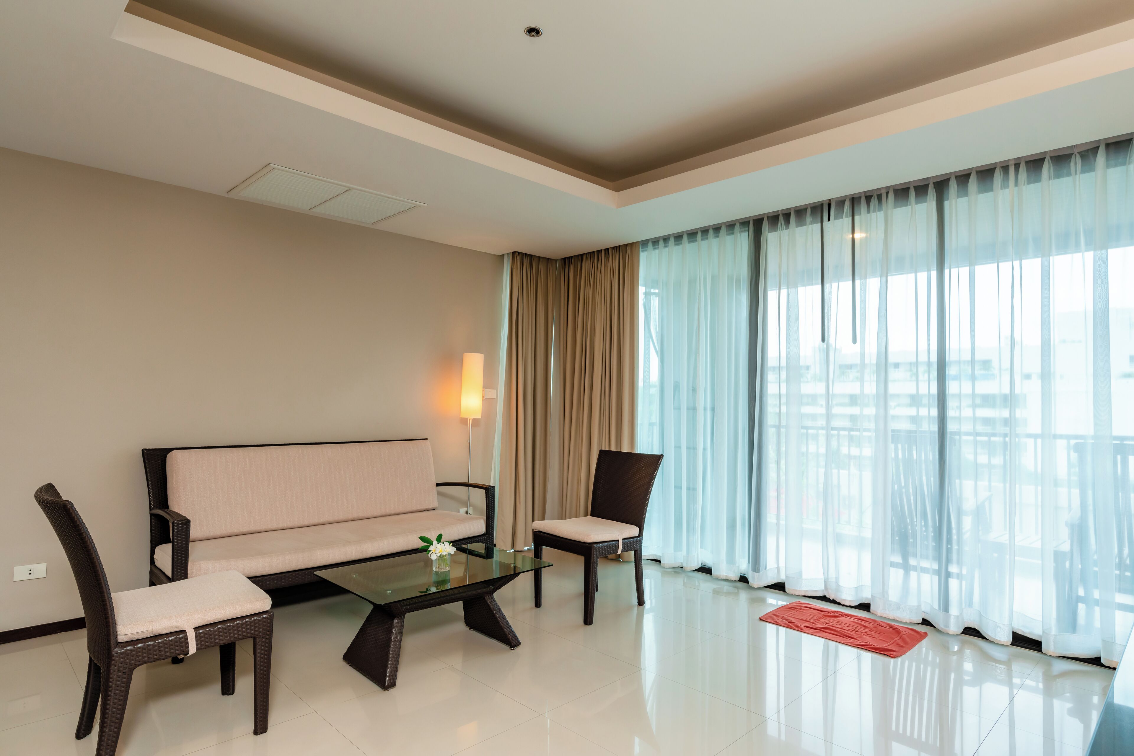 Una sala de estar moderna con un sofá, dos sillones, una mesa de centro de vidrio y vistas a través de cortinas translúcidas.