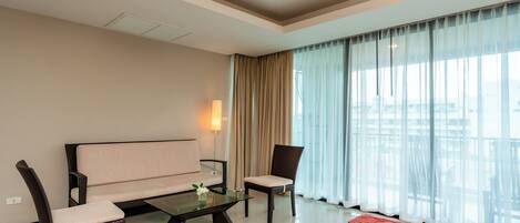 Una sala de estar moderna con un sofá, dos sillones, una mesa de centro de vidrio y vistas a través de cortinas translúcidas.