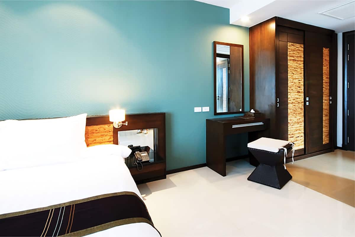 Quarto de hotel com uma cama, escrivaninha, cadeira, espelho e guarda-roupa.