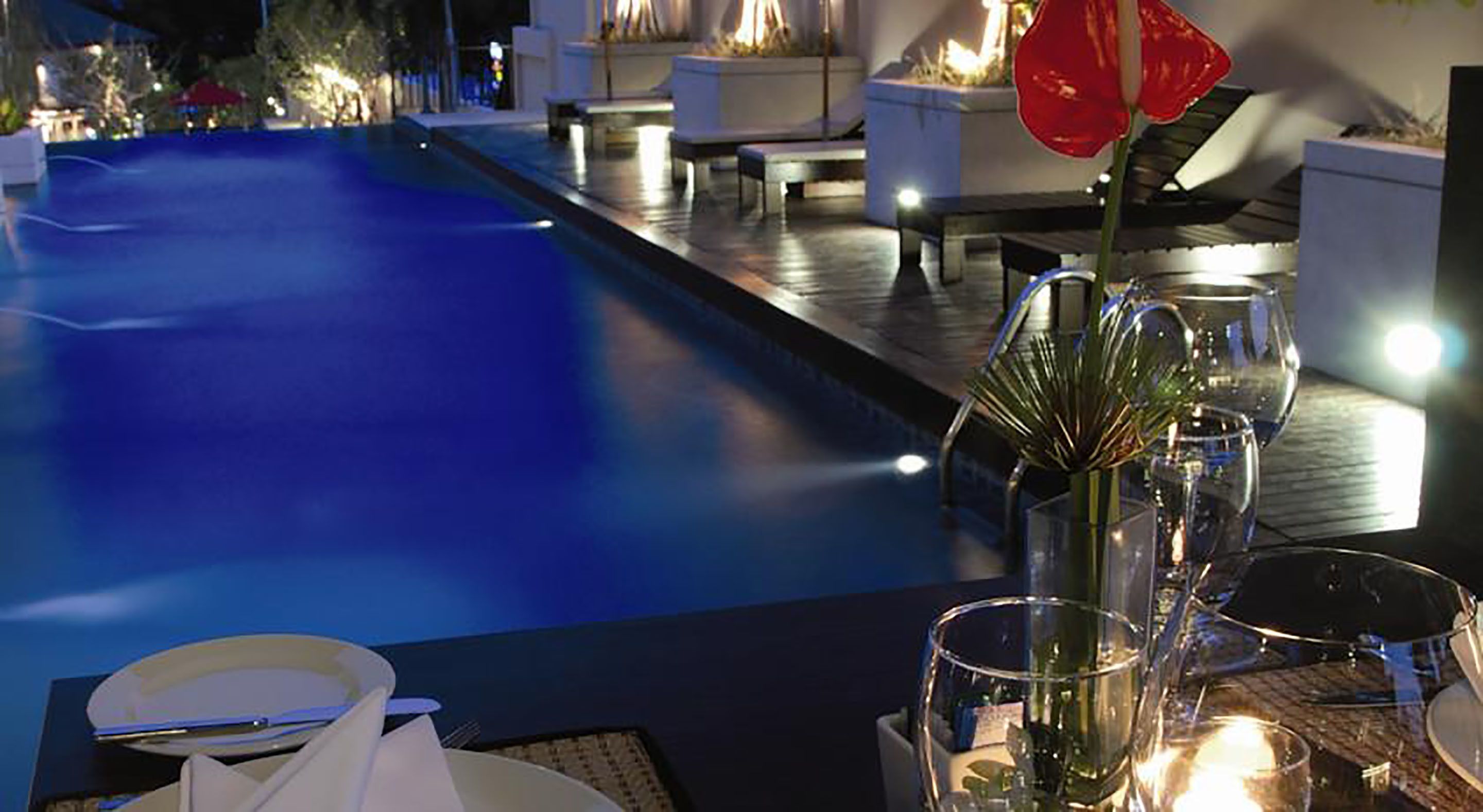 A poolside area with a dining setup, including a table with chairs and a vase of flowers.