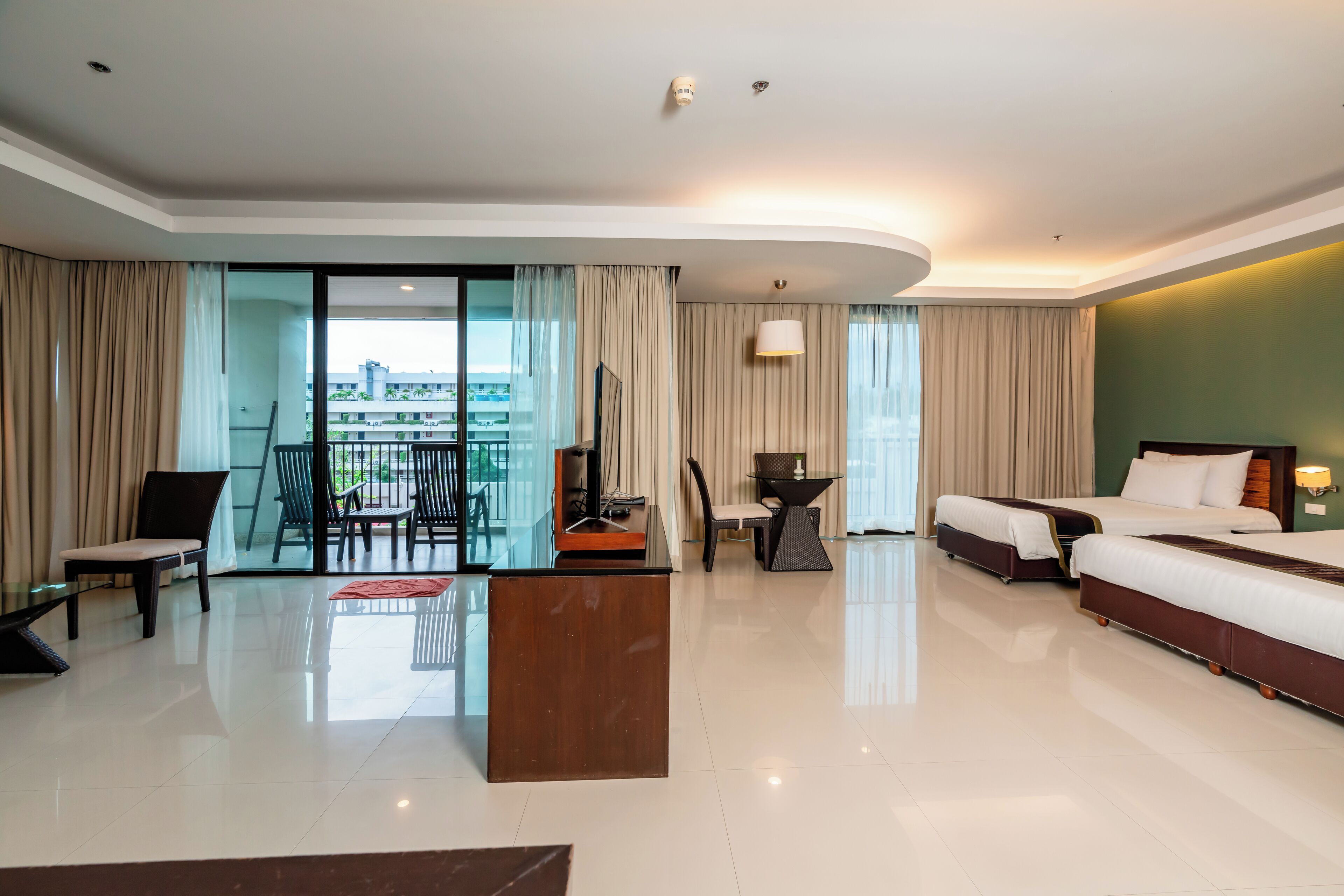 A modern hotel room with a large bed, a sofa, a dining area, and a balcony with a view of the city.