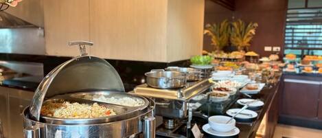 A buffet setup with various food items and a large pot of rice in the foreground.