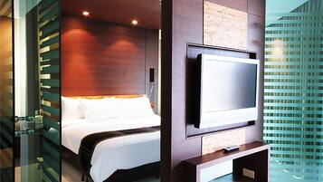 Una habitación de hotel moderna con una cama grande, un televisor de pantalla plana montado en la pared y un separador de vidrio.