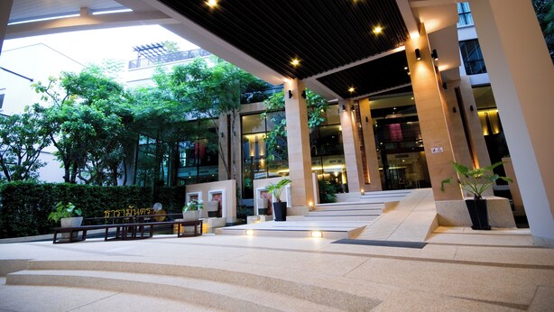 A modern building entrance with a covered walkway, potted plants, and steps leading to the entrance. - Tara Mantra Cha Am Resort (Cha-am)