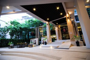 A modern building entrance with a covered walkway, potted plants, and steps leading to the entrance. - Tara Mantra Cha Am Resort (Cha-am)