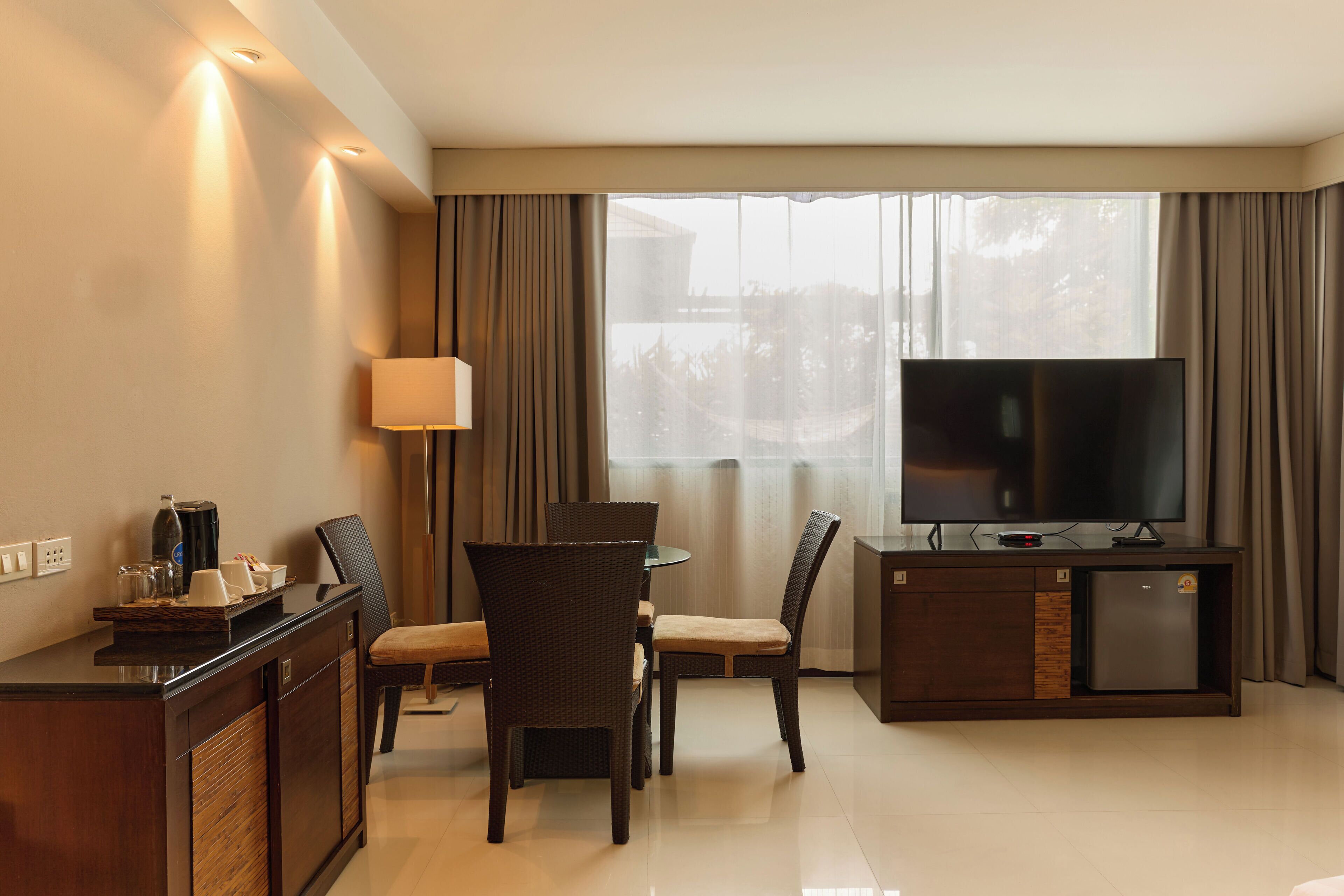 A hotel room with a dining area, a TV, a coffee machine, and a minibar.