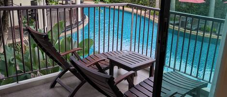 A balcony with a view of a swimming pool, wooden furniture, and a railing.