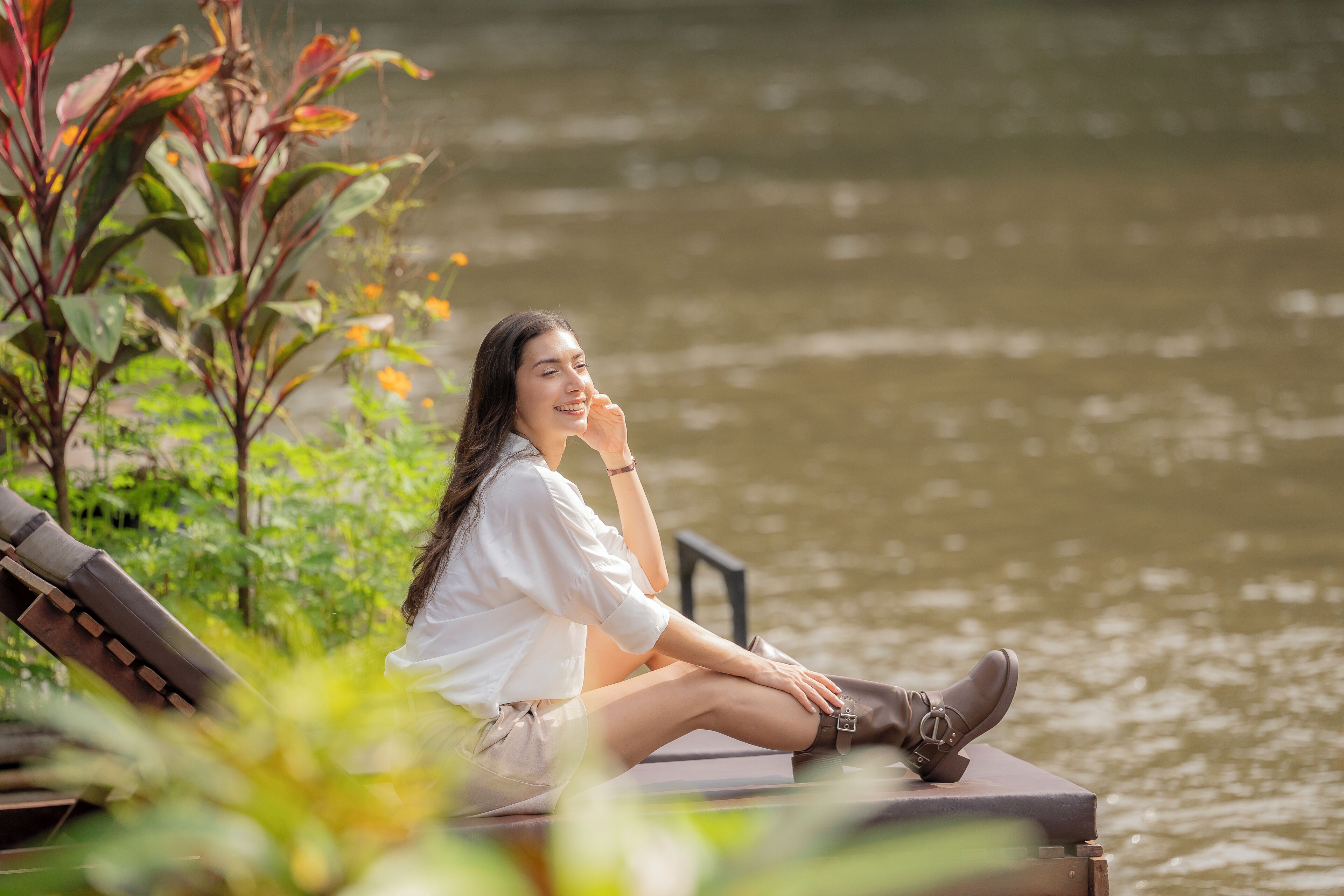A person sitting on a bench by a body of water, surrounded by greenery.