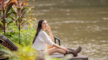 A person sitting on a bench by a body of water, surrounded by greenery.