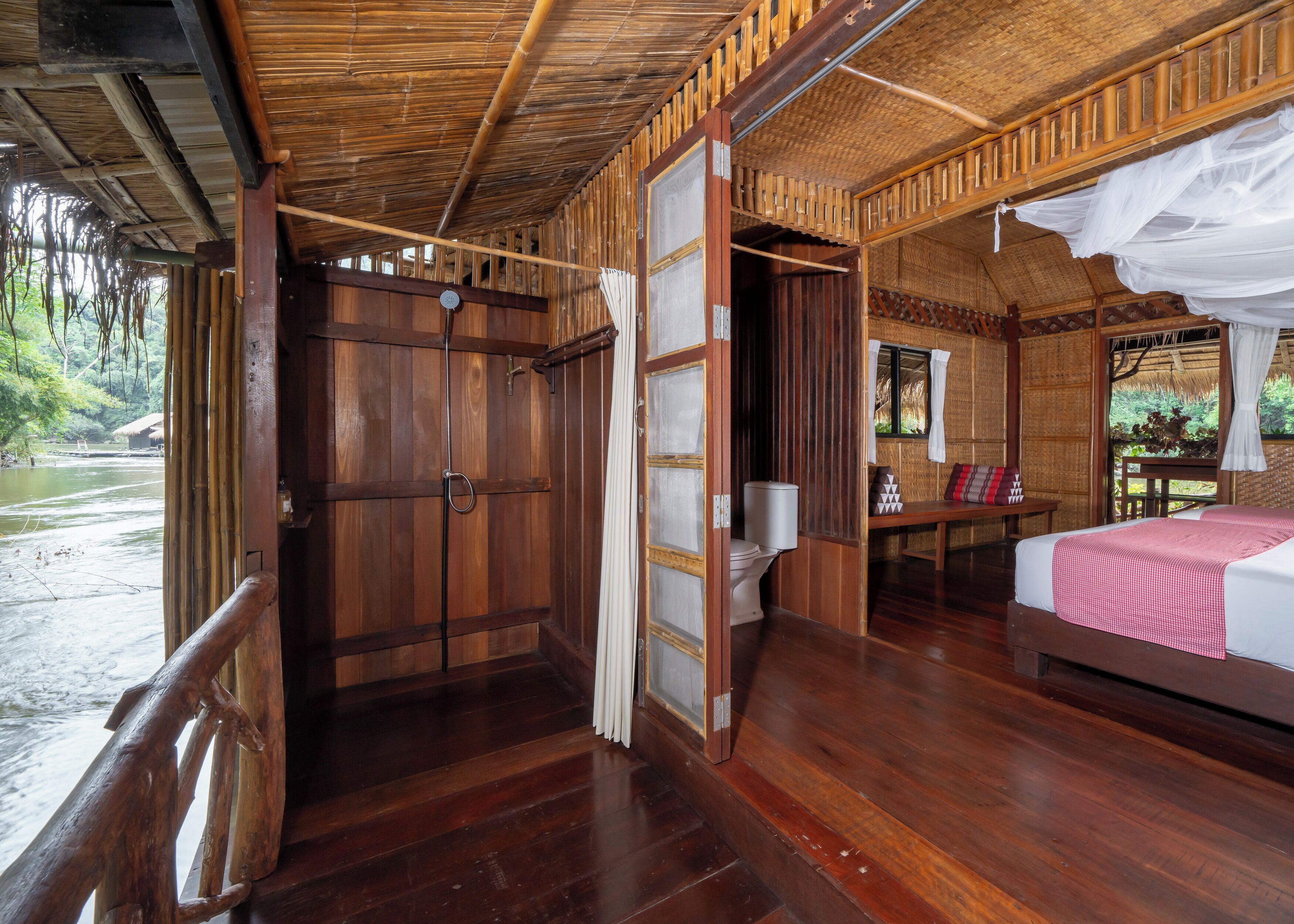 Een houten kamer met een bed, toilet en een raam met uitzicht op een rivier.