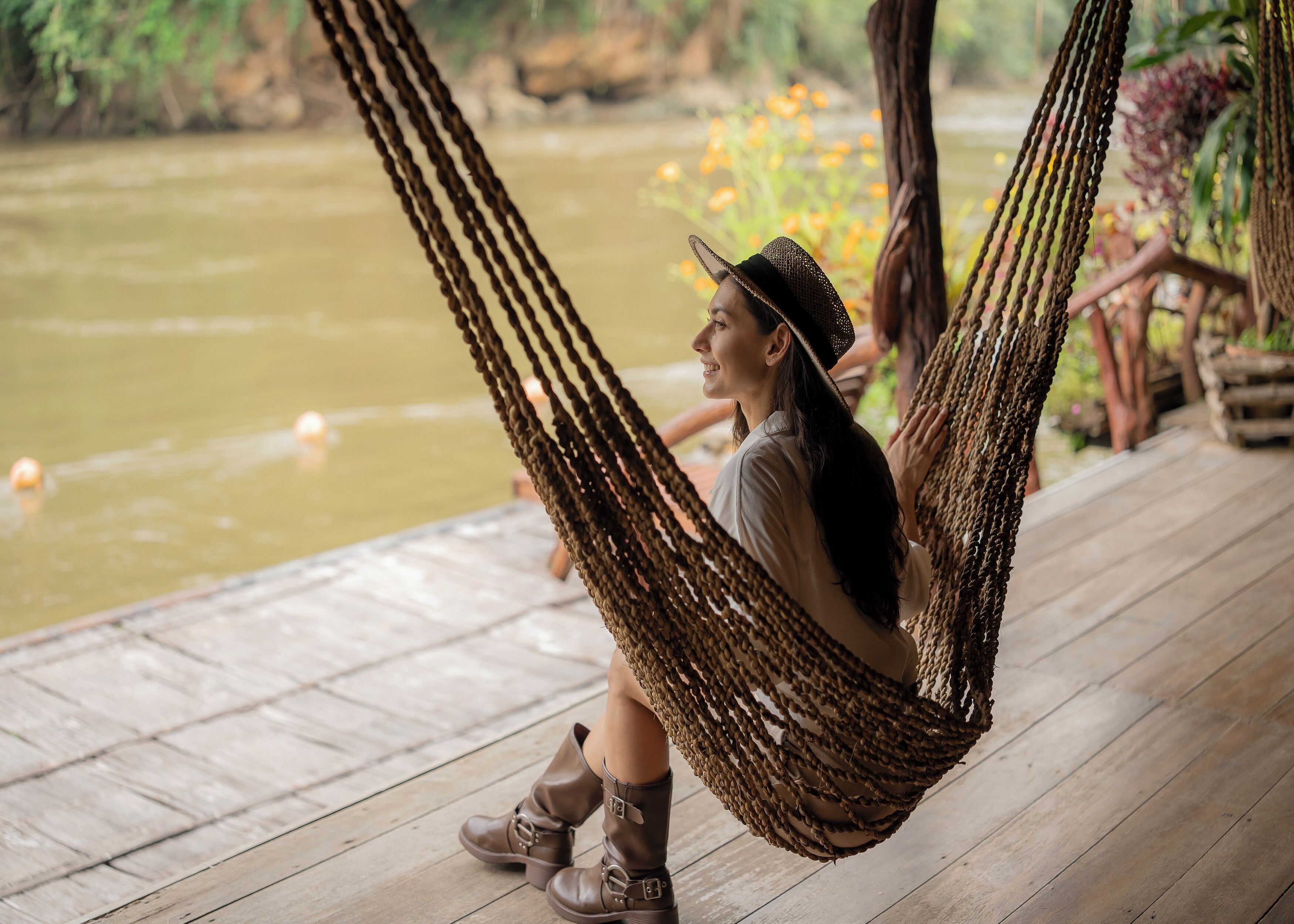 A person relaxing in a hammock on a wooden deck by a body of water.