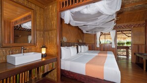 A wooden room with a bed, a bedside table with a lamp, and a large mirror. - River Kwai Jungle Rafts (Sai Yok)