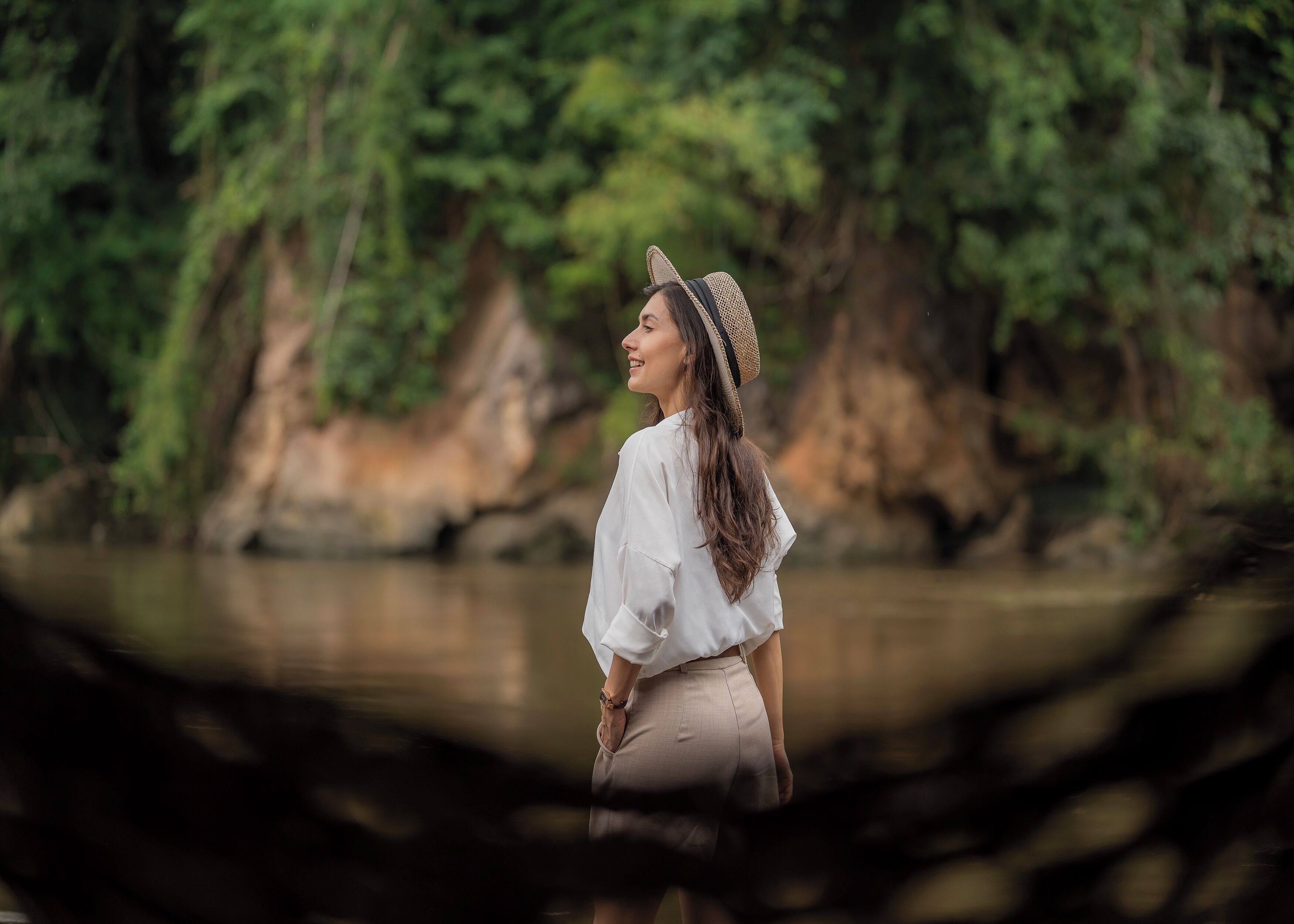 A person standing by a river with a natural backdrop of trees and rocks.