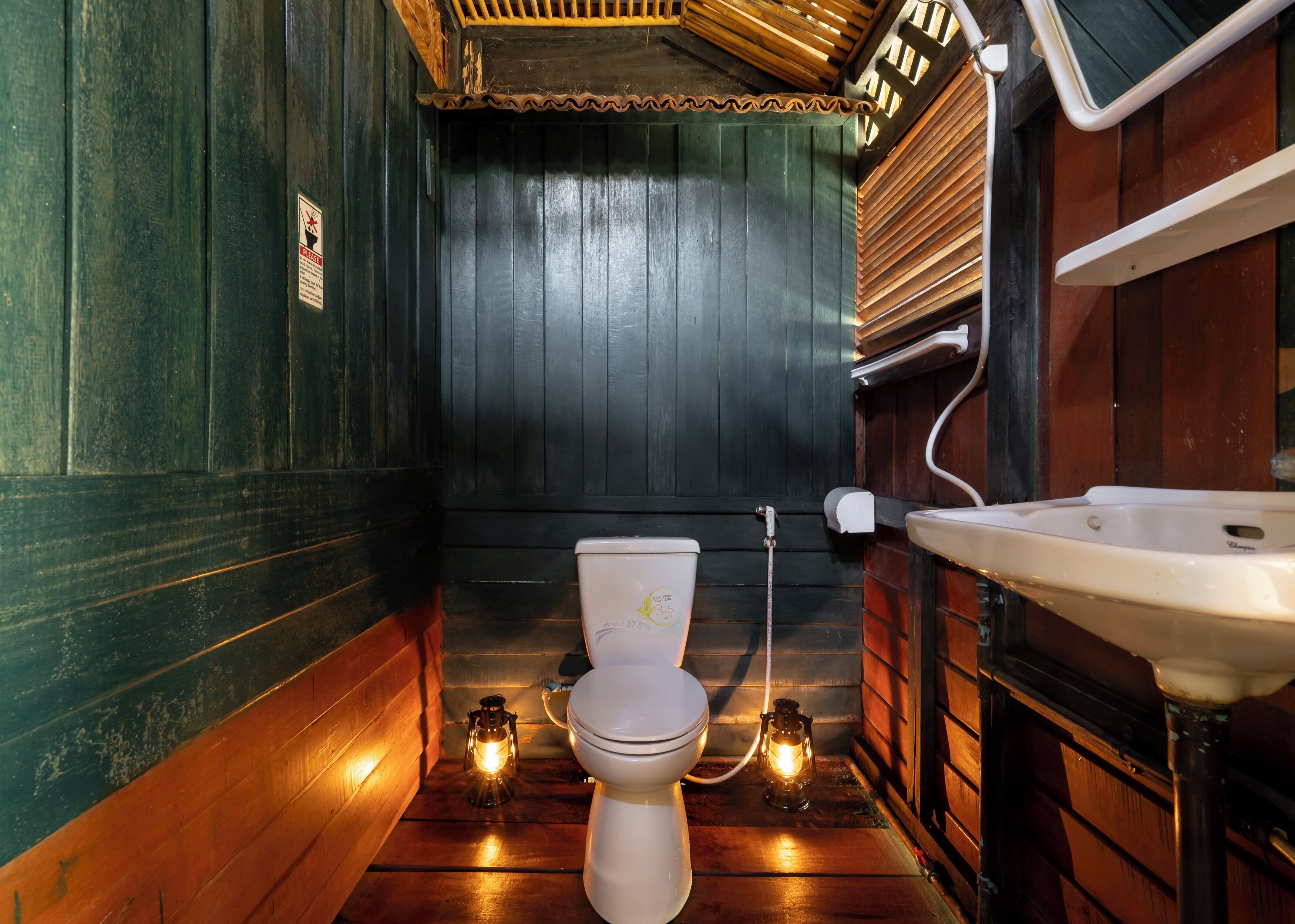 Un baño estrecho con paneles de madera, un inodoro blanco, un lavabo y dos faroles iluminados en el suelo.