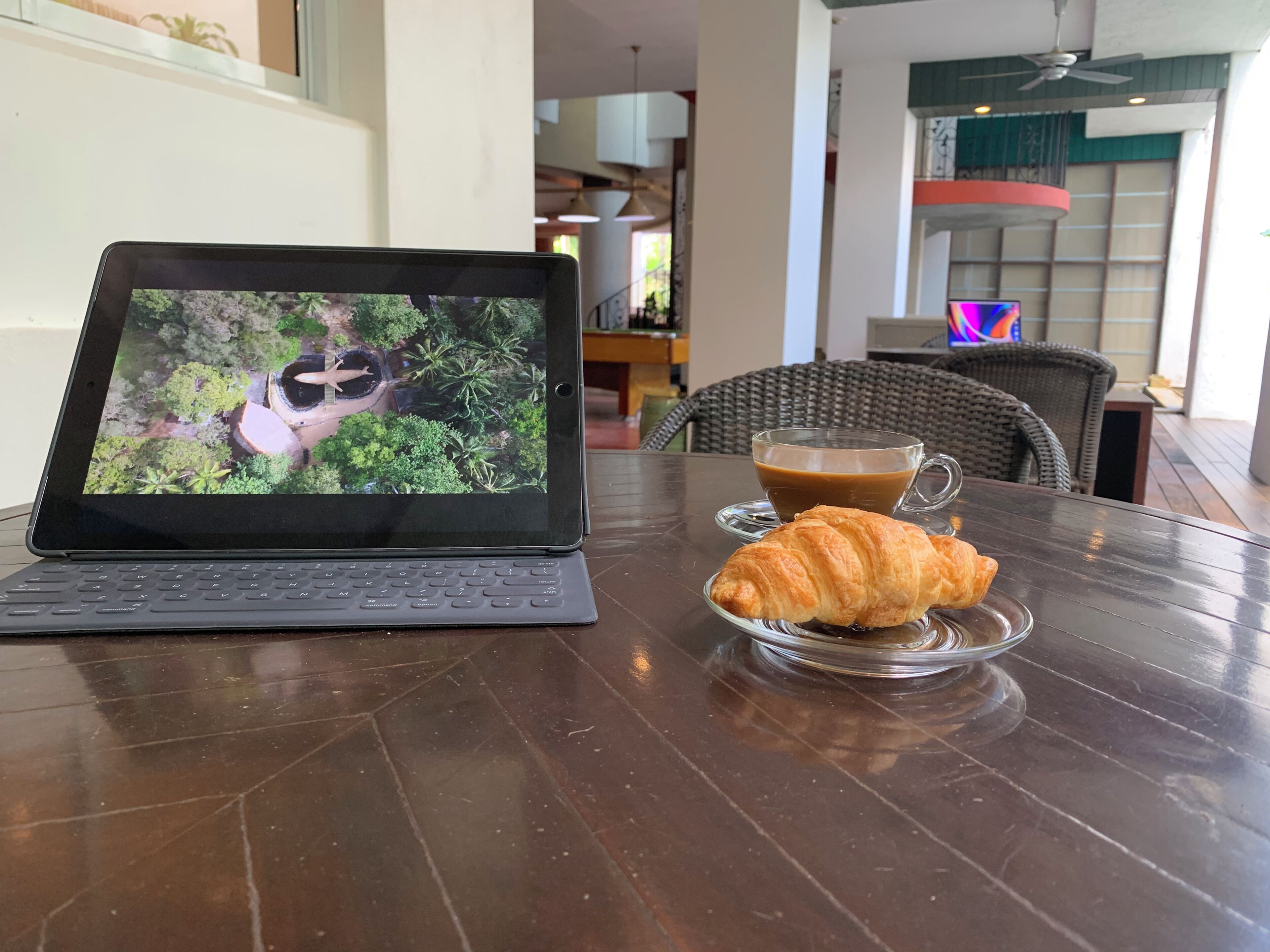 A laptop displaying a nature scene, a cup of coffee, and a croissant on a table.