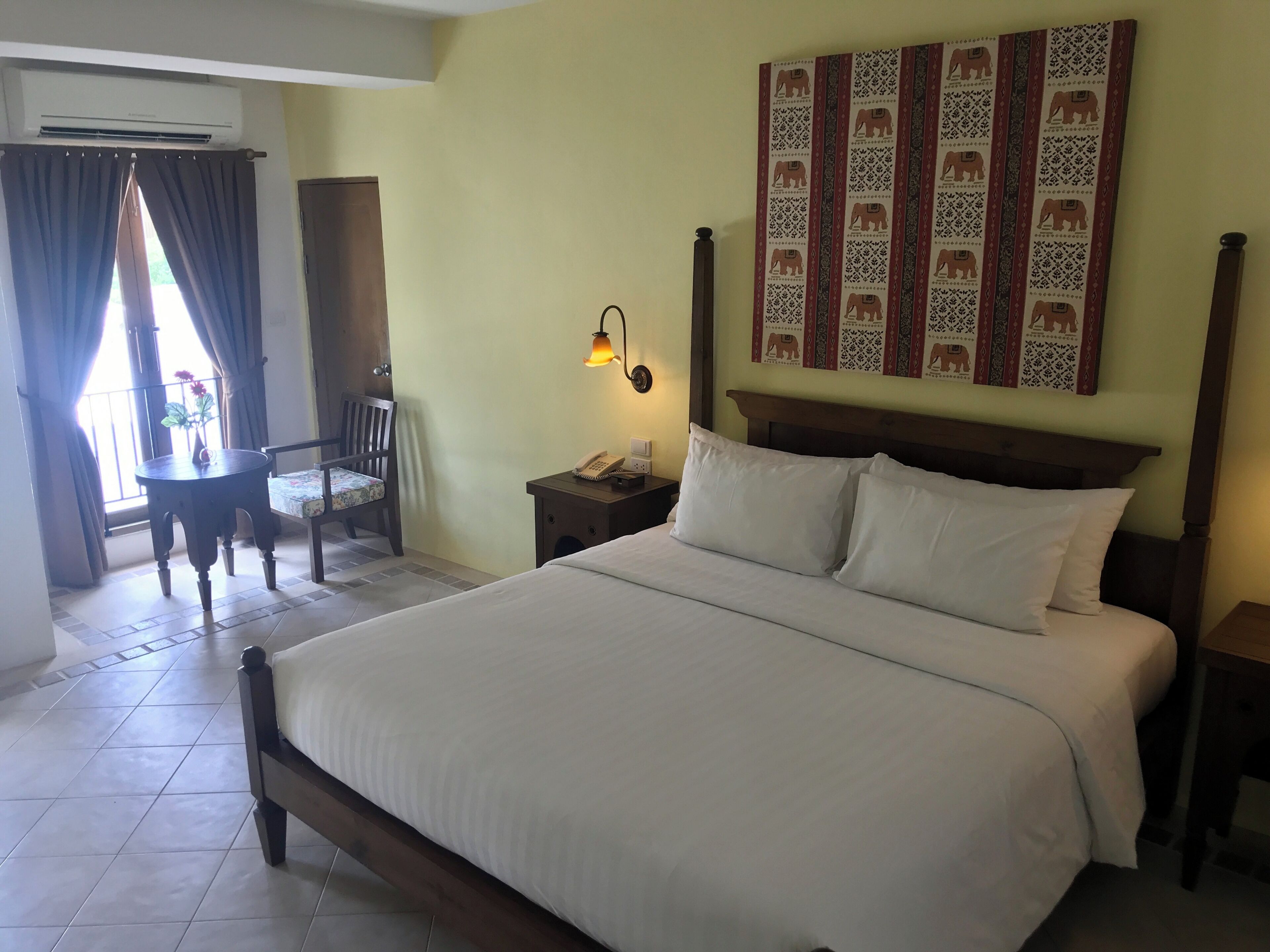 Habitación de hotel con cama, escritorio, silla, mesita de noche, lámpara y una pared decorada con diseños.