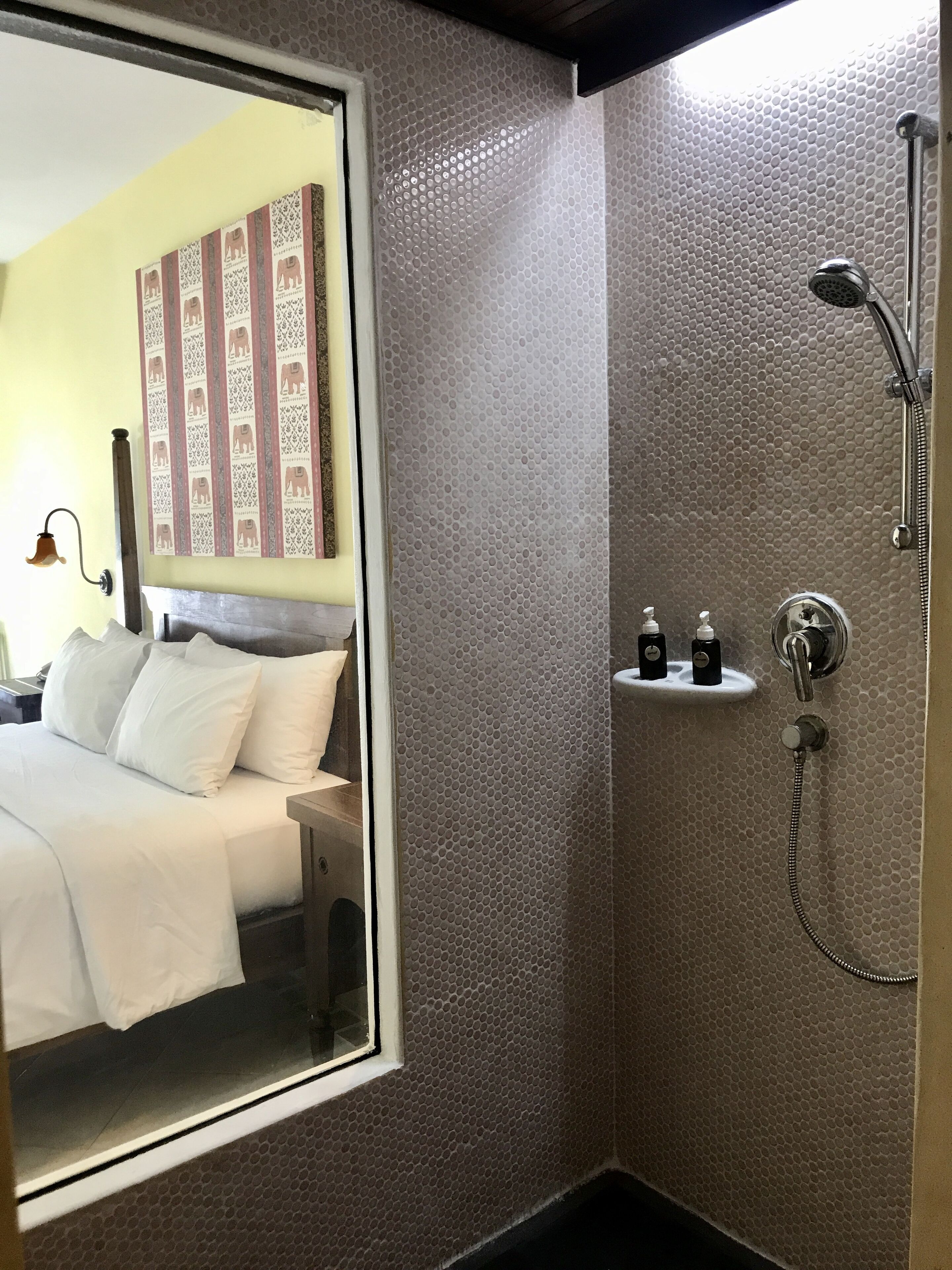 Un baño de hotel con ducha, cama con ropa blanca y pared con diseño estampado.