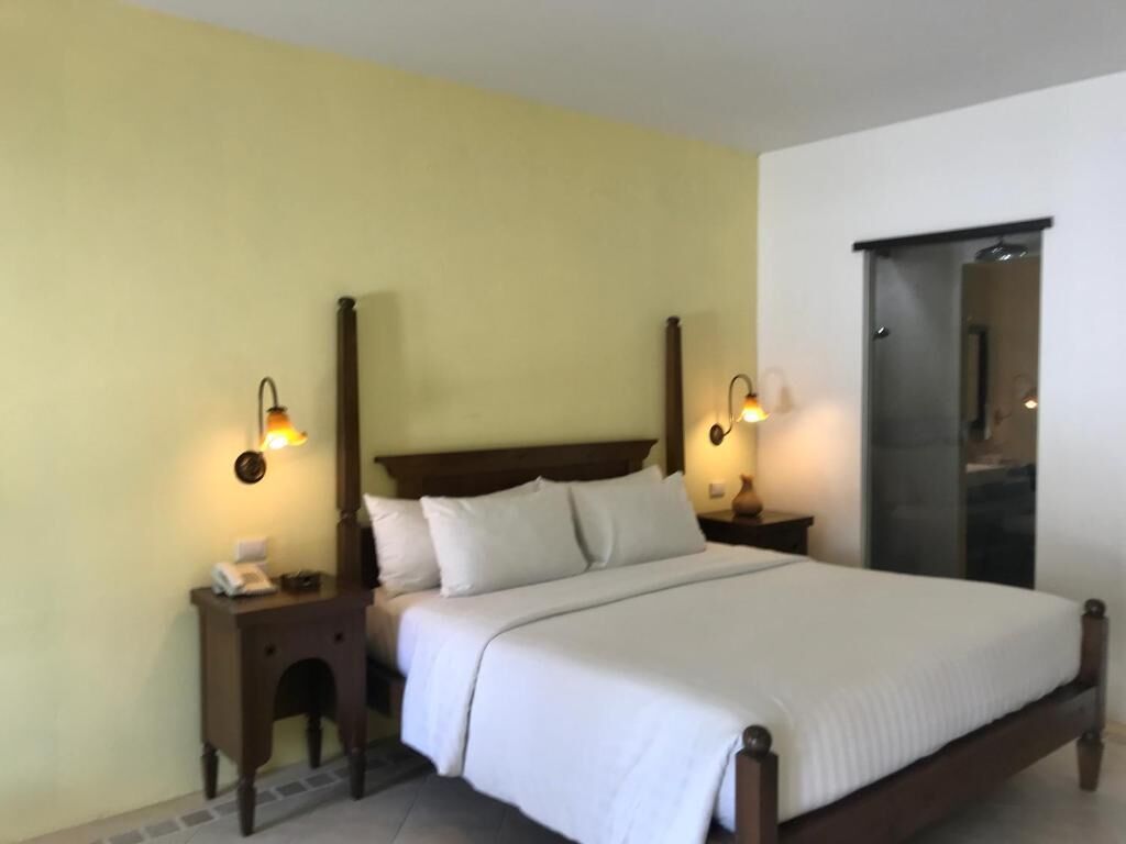 Una habitación de hotel estándar con una cama individual, dos mesitas de noche y lámparas fijadas a la pared.