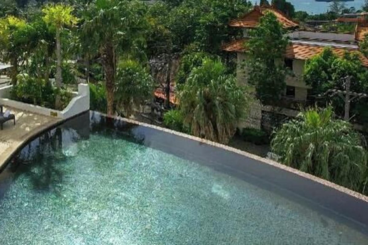 A swimming pool with a curved edge, surrounded by greenery and buildings with red-tiled roofs.