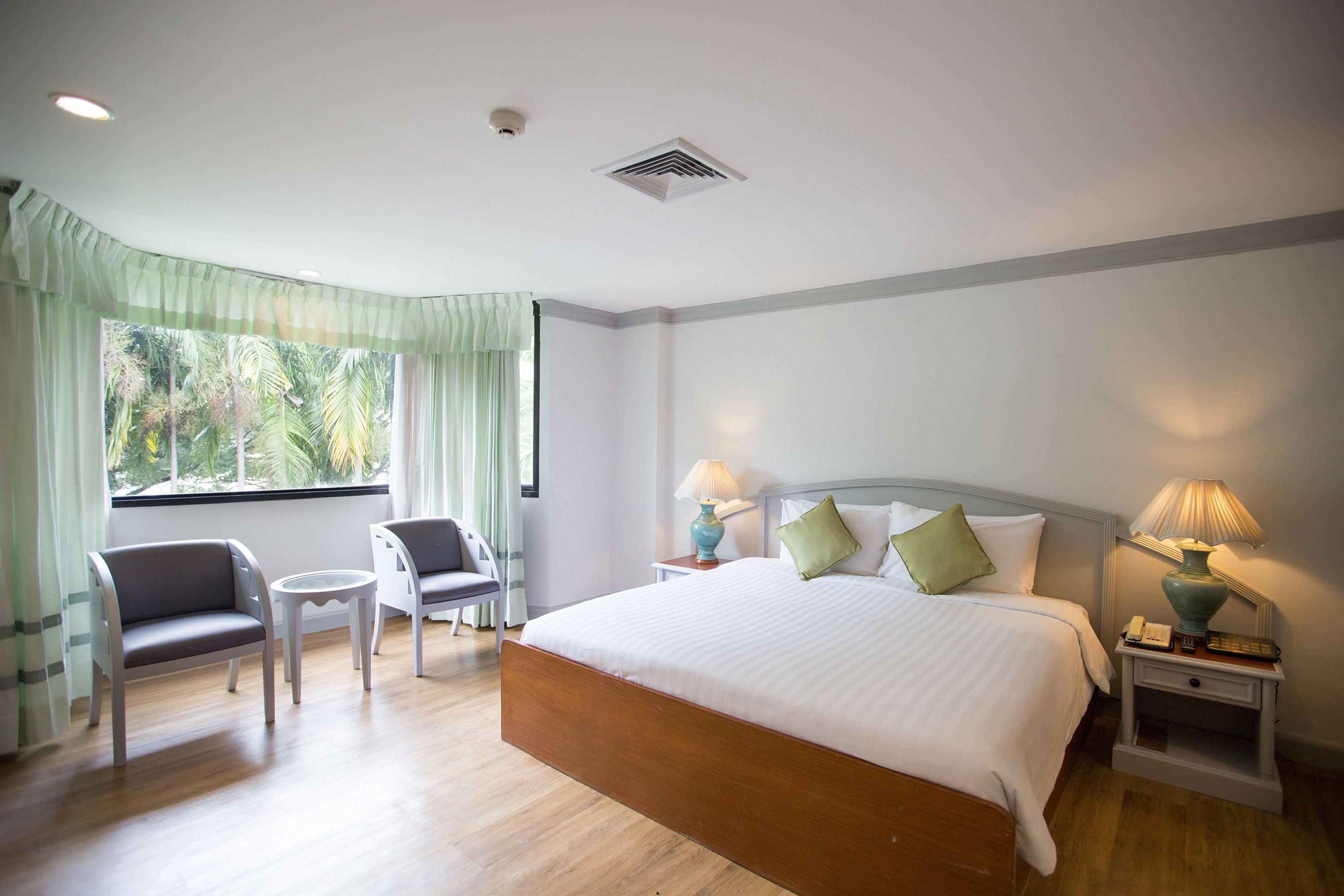 A hotel room with a large bed, two chairs, a small table, and a nightstand with lamps.