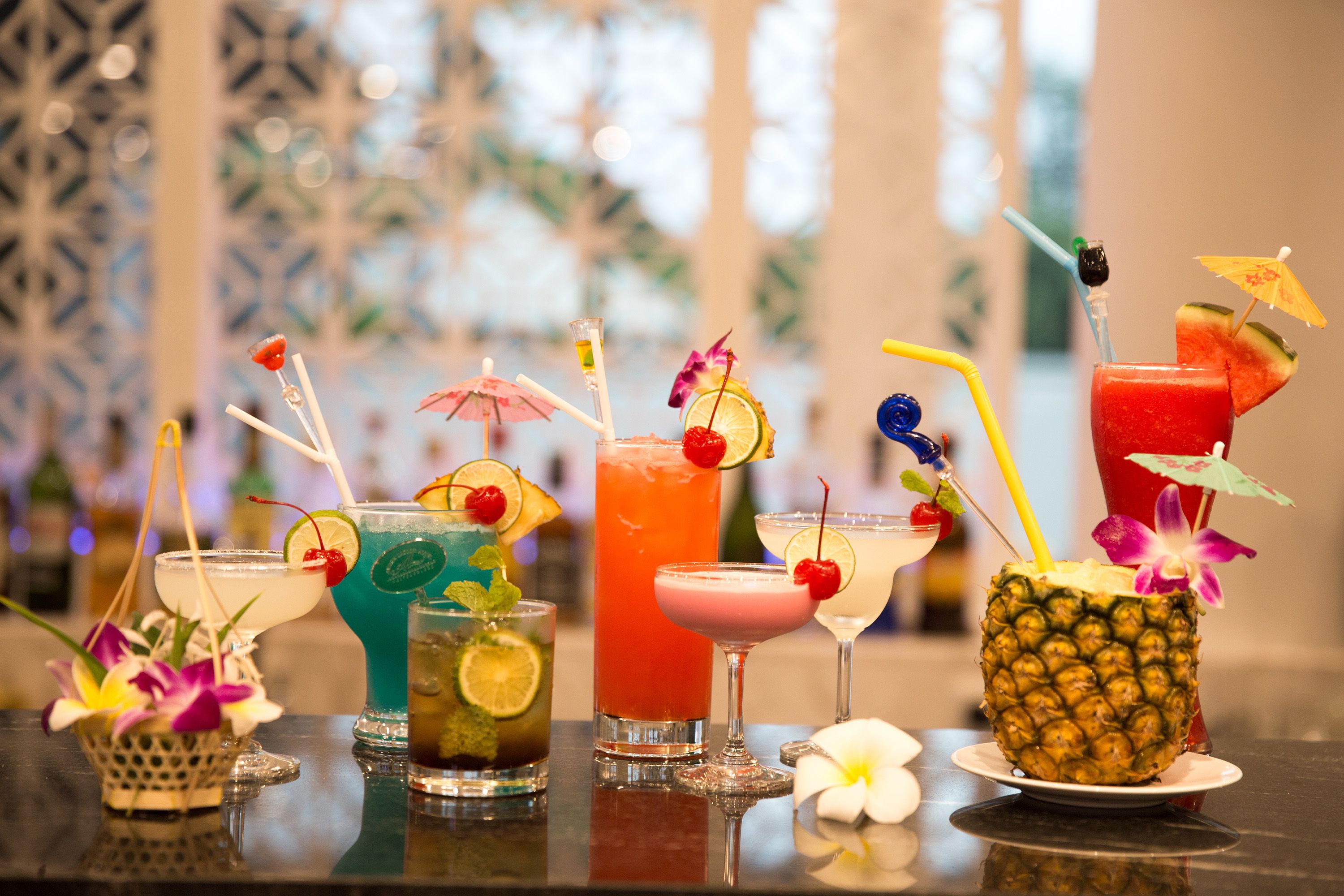A variety of cocktails on a bar counter with decorative elements like umbrellas and cherries.