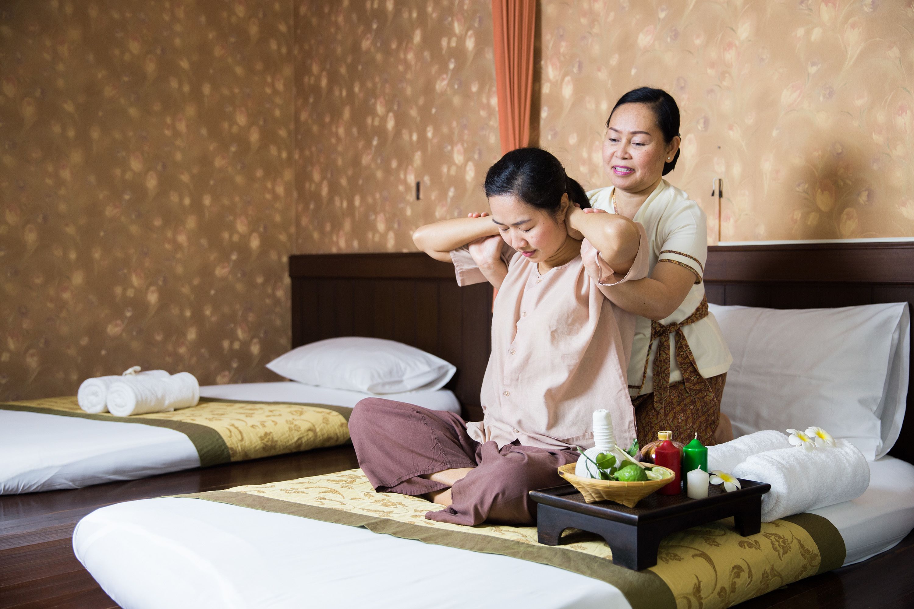 A room with two beds, one with a rolled towel and the other with a tray of toiletries.