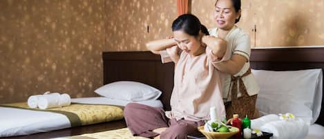 A room with two beds, one with a rolled towel and the other with a tray of toiletries.