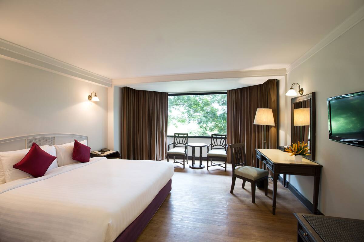 A hotel room with a large bed, a desk with a chair, a small table, and a TV on the wall.