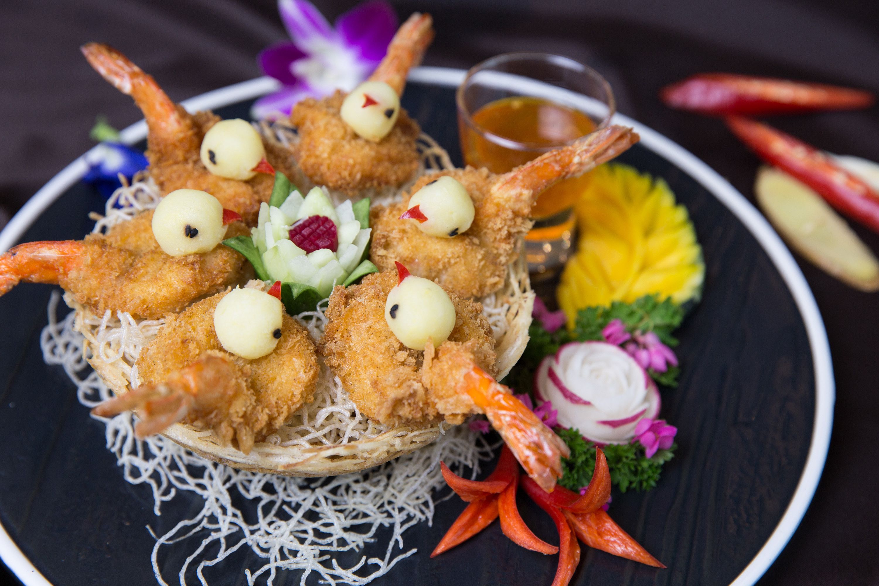 A plate of fried shrimp garnished with vegetables and a small bowl of sauce.