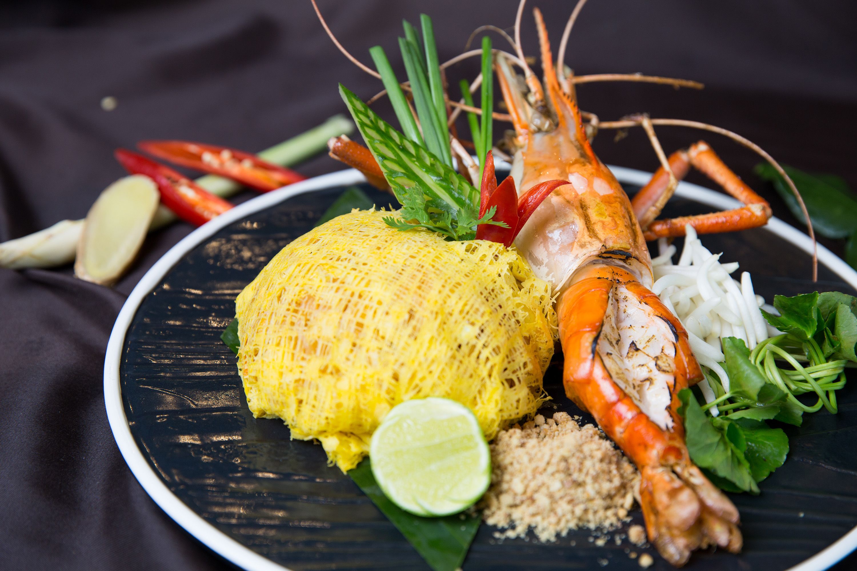 A plate with a lobster, corn, lime, and various vegetables.
