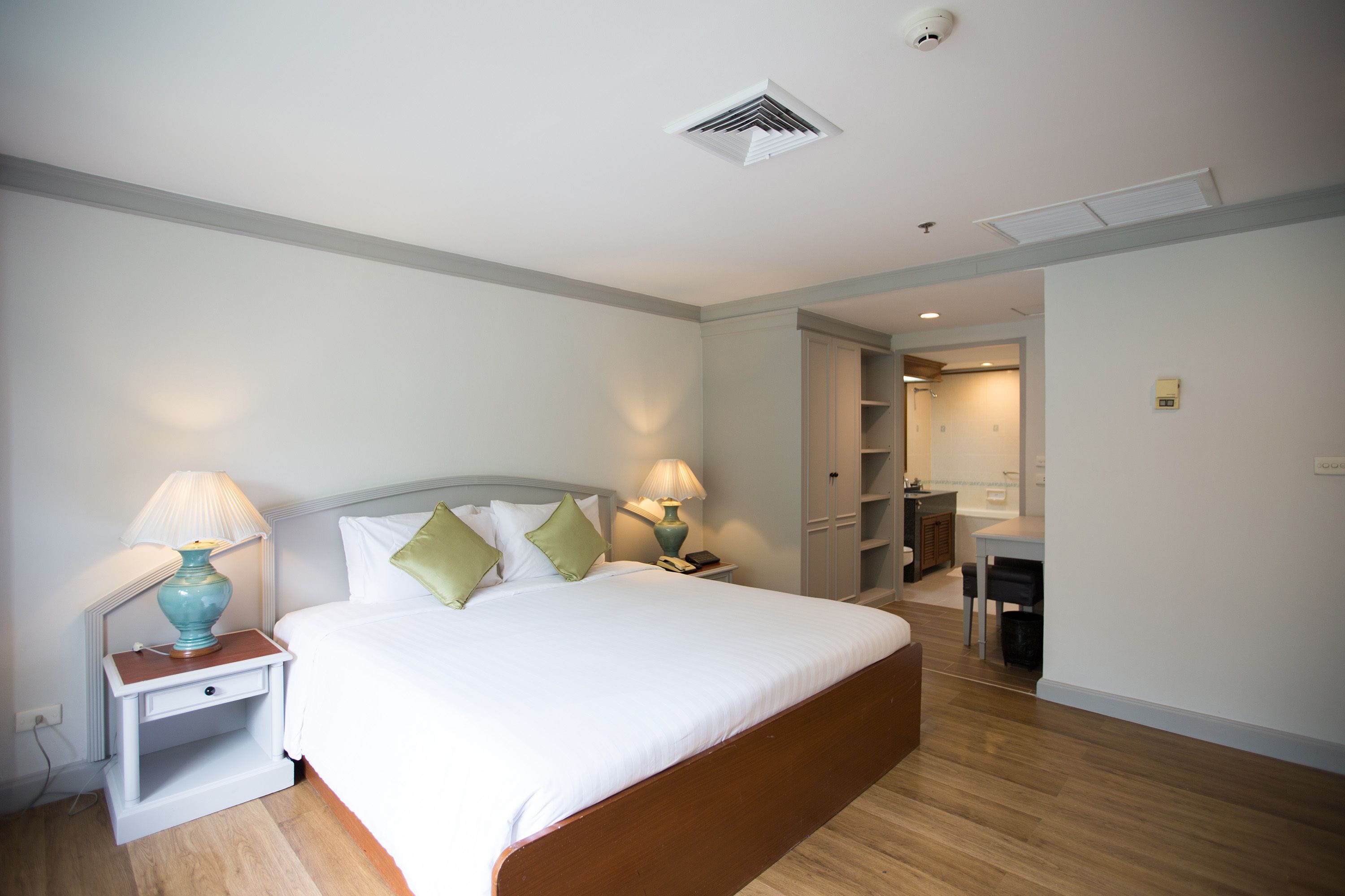 Habitación de hotel con una cama grande, dos mesitas de noche con lámparas, un armario y una pequeña zona de kitchenette.