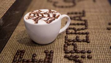 A white cup with a latte art design on a textured surface with coffee beans arranged in letters.