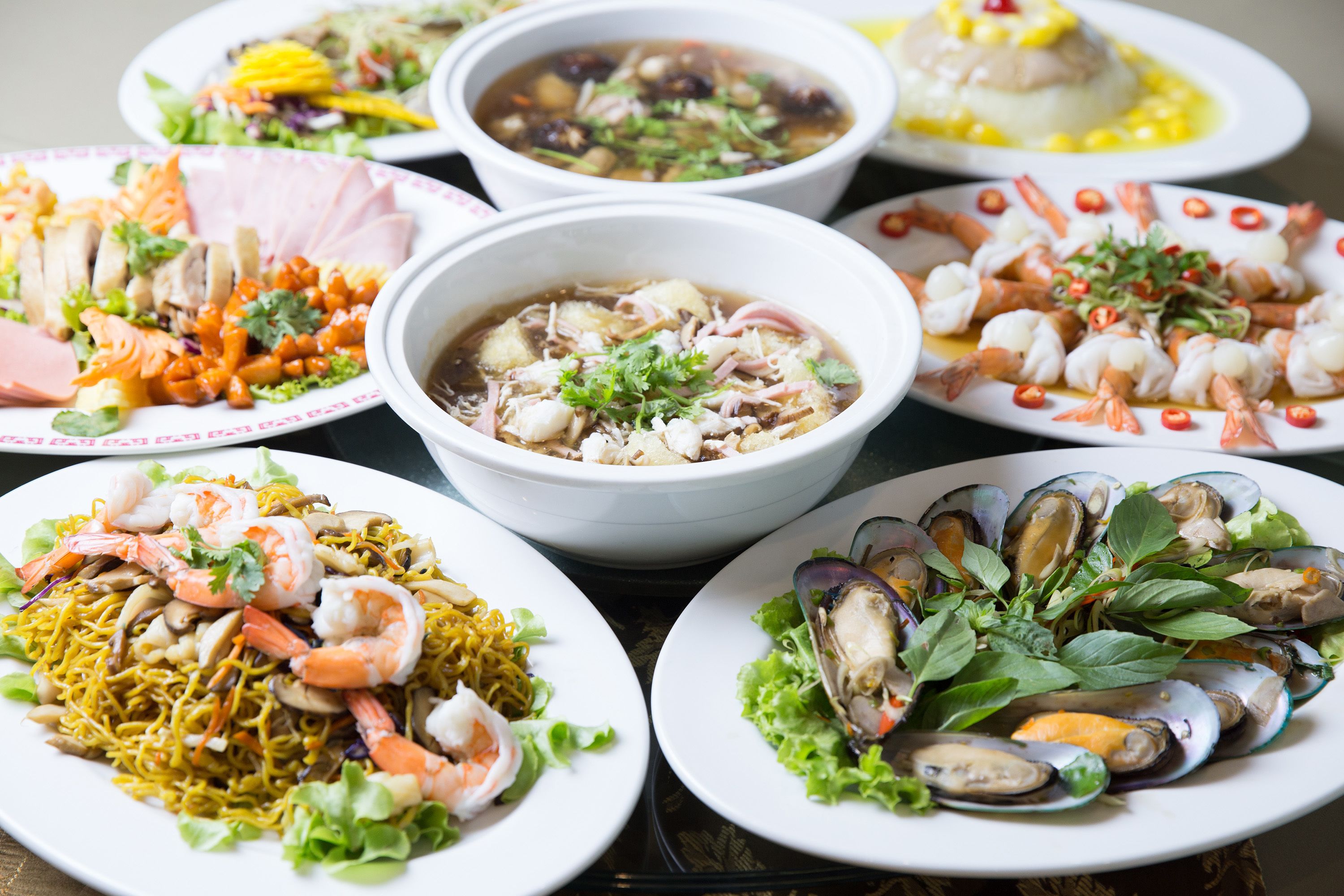 Variedad de platos que incluyen mariscos, fideos y ensaladas, lo que sugiere una amplia oferta gastronómica.