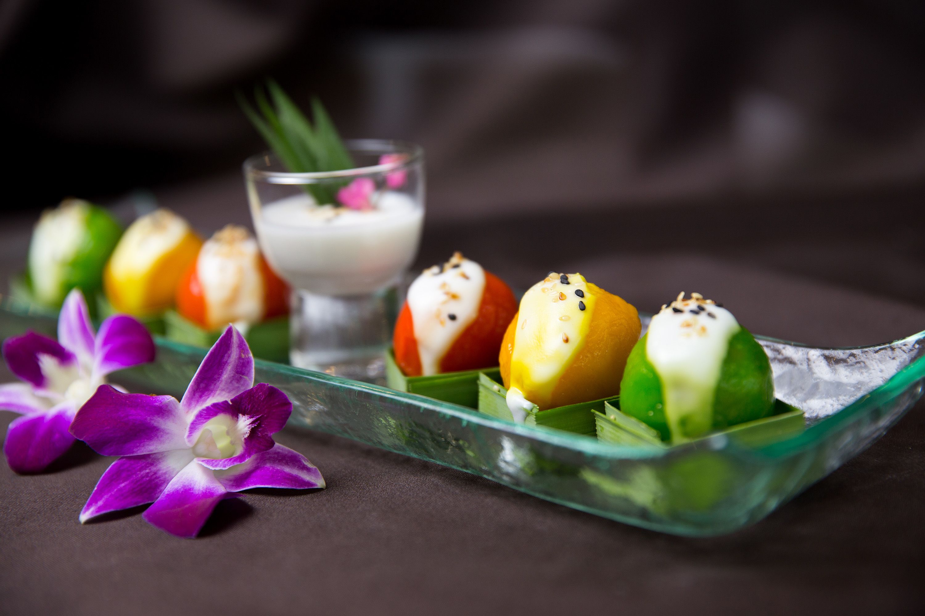 Un plat en verre contenant des fruits aux couleurs vives et une orchidée violette.