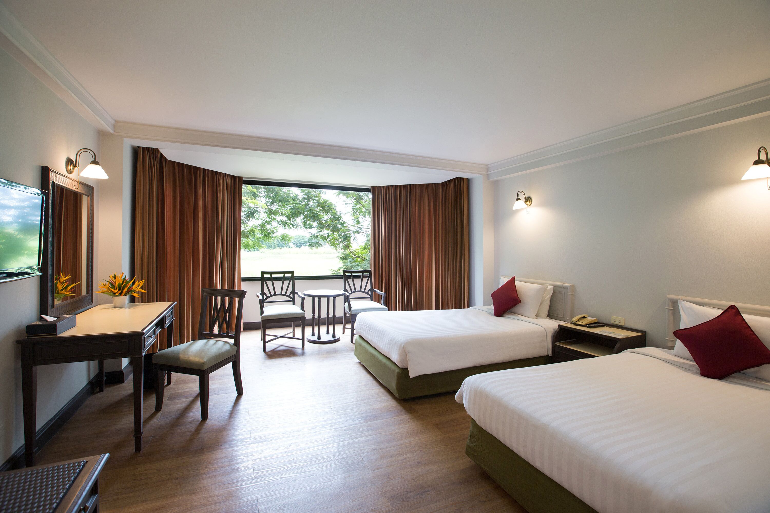 A hotel room with two beds, a desk, a chair, a small table, and a TV.