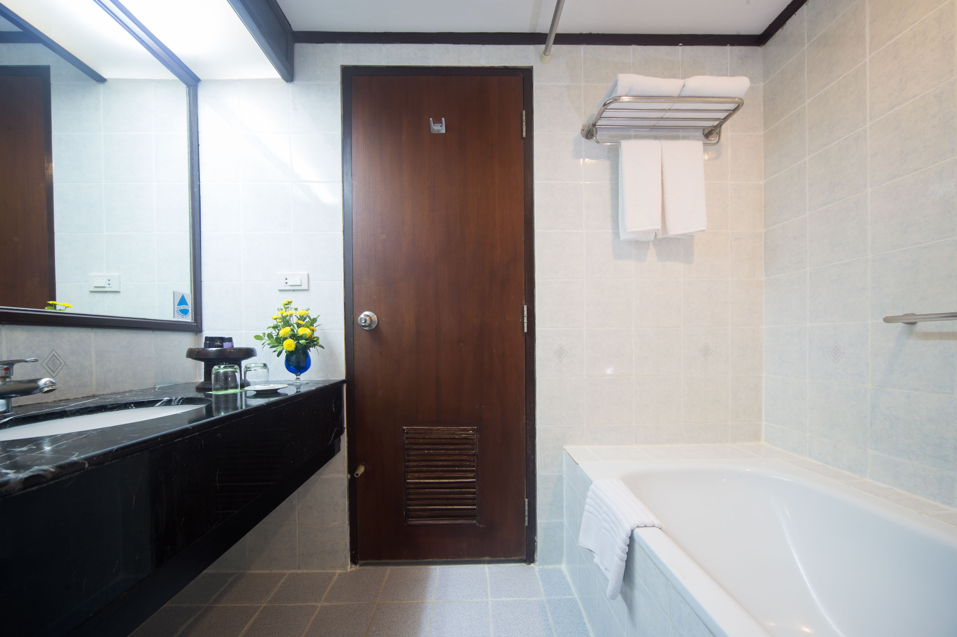 A modern bathroom with a wooden door, a bathtub, and a large mirror.