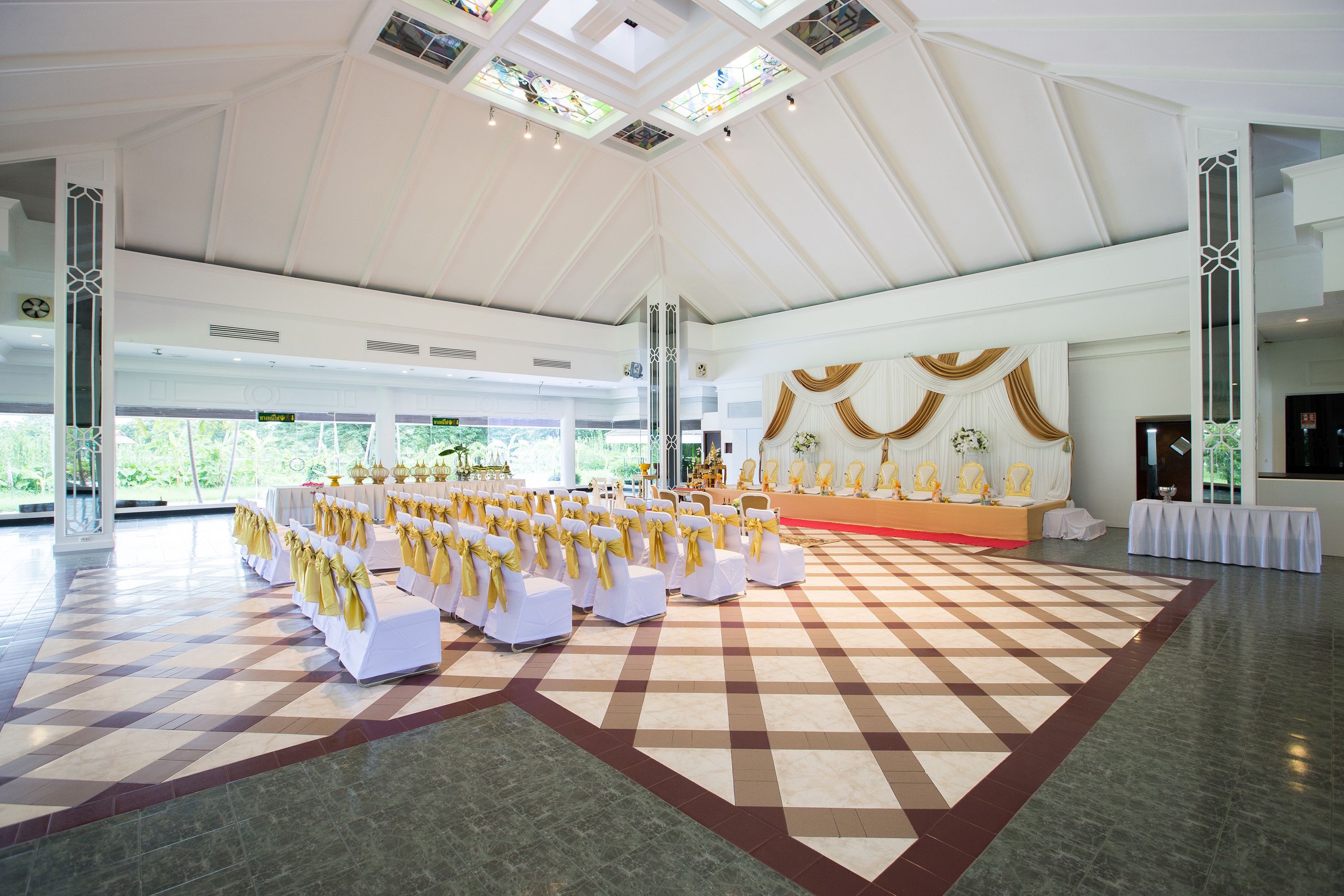 A spacious hall with a high ceiling, a checkered floor, and rows of white chairs with yellow sashes.