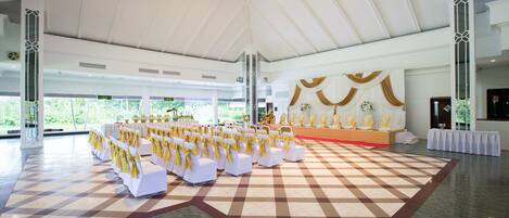 A spacious hall with a high ceiling, a checkered floor, and rows of white chairs with yellow sashes.