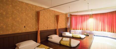 Habitación de hotel con tres camas, piso de madera y un ventanal con cortinas rojas.