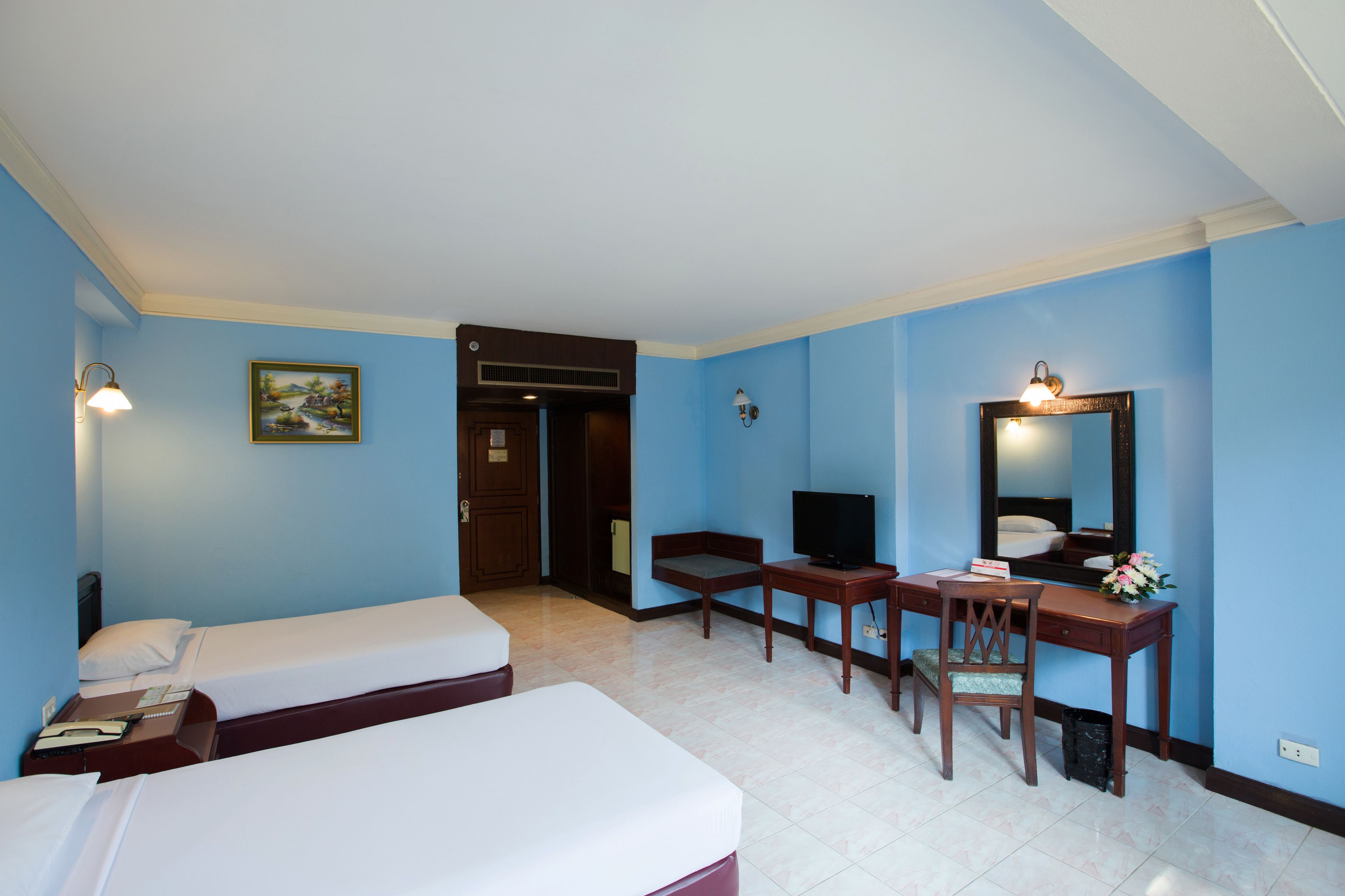 A hotel room with two single beds, a desk with a chair, a television, a mirror, and a painting on the wall.