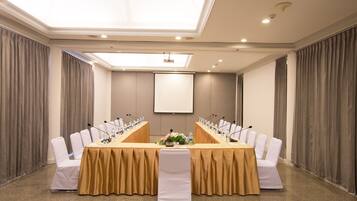 A conference room with a long table, white chairs, microphones, and a projector screen.