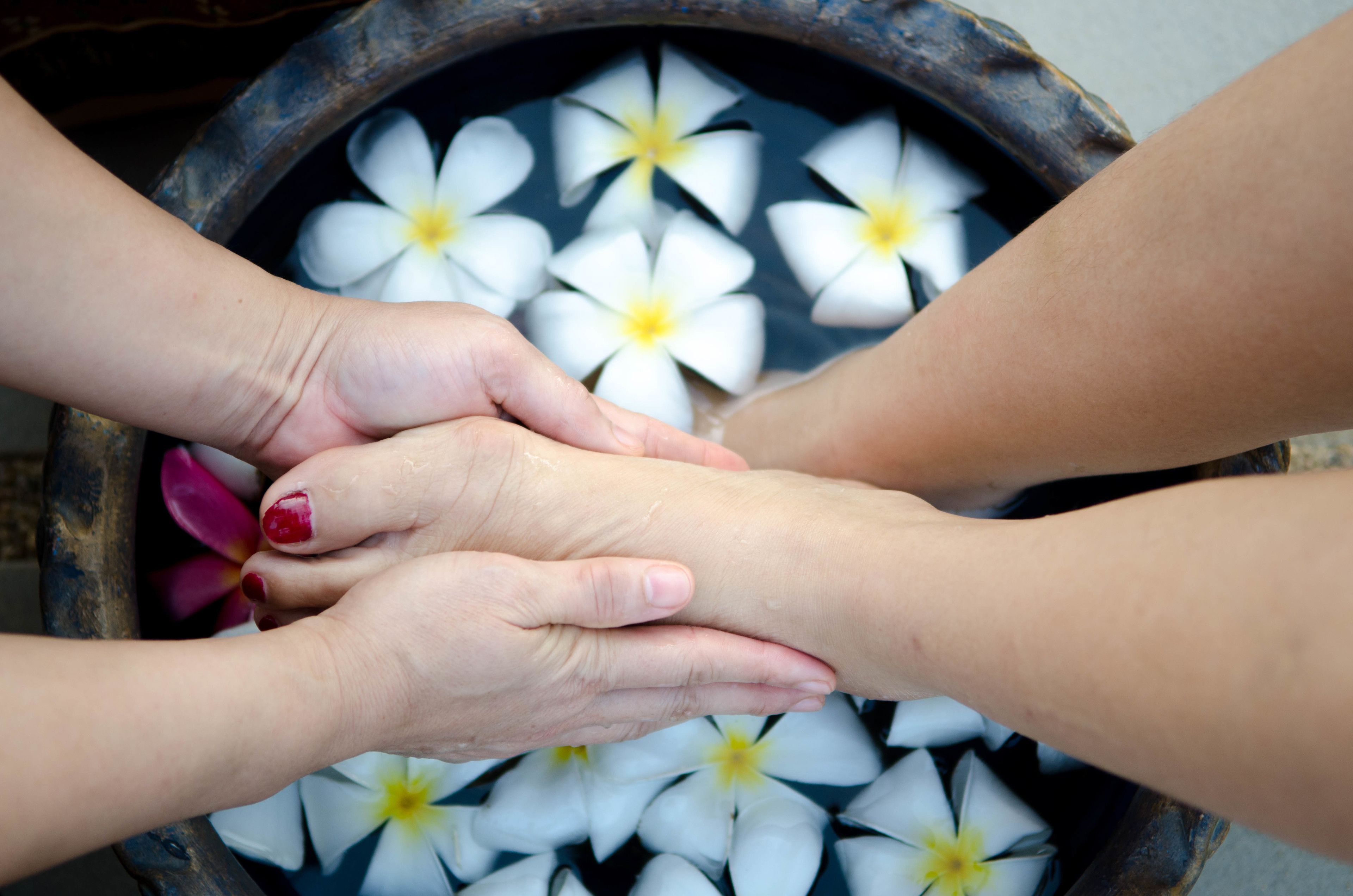 Due mani appoggiate su una superficie con fiori bianchi e un oggetto scuro sullo sfondo.