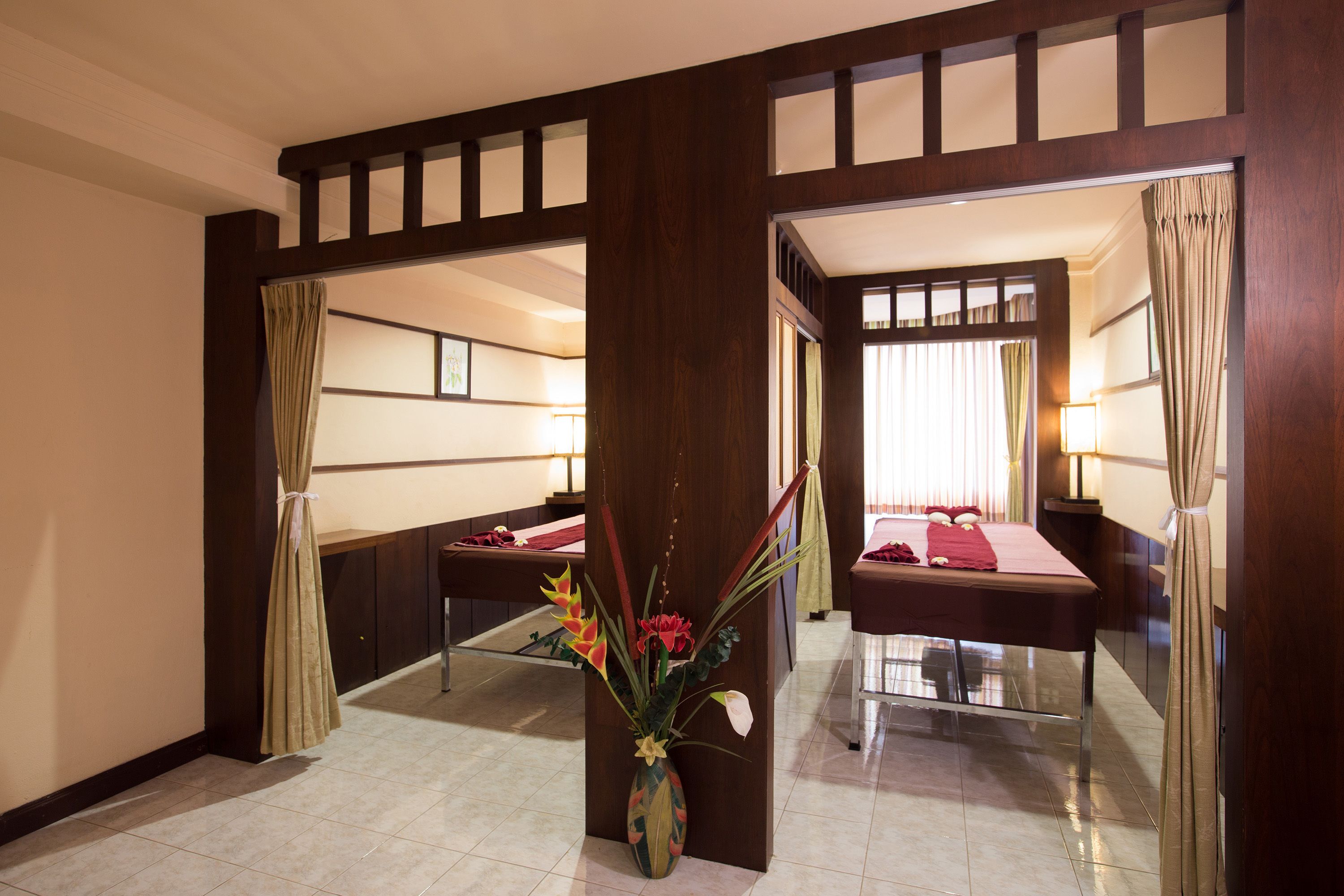A hotel room with a large bed, a small table, a vase with flowers, and a mirror.