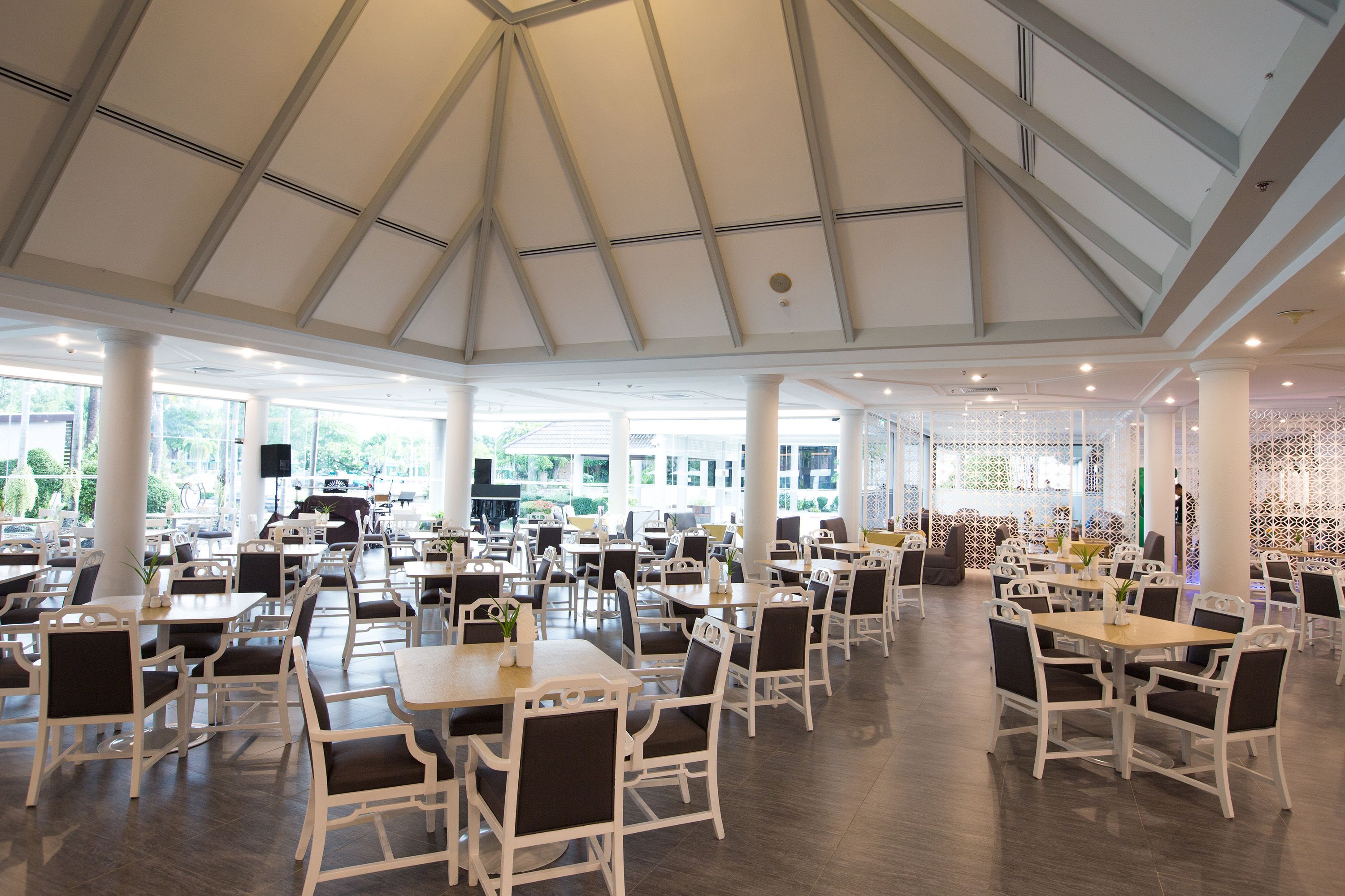 A spacious dining area with white tables and chairs, large windows, and a high ceiling.